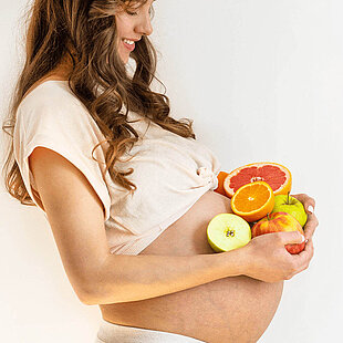 A pregnant woman holds fruits on her belly.