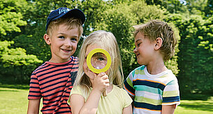 Three children outdoors, one looking through a magnifying glass.