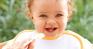 A baby with curly hair is being fed with a spoon.