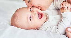 A woman lovingly kisses a laughing baby.
