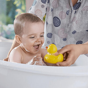 Baby laughing in bathtub with toy duck.