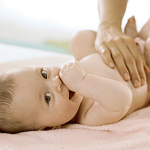 Baby lying on a pink towel, being attended to by an adult's hand.