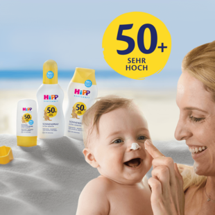 A woman applies sunscreen to a laughing baby on a beach, with three bottles of 'Hipp BabySanft' sunscreen in the background.