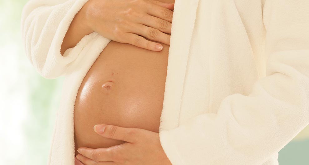 A pregnant woman in a white robe, gently cradling her belly.