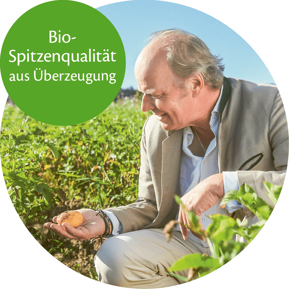 An elderly man in a field holds a potato, with a green bubble containing German text nearby.