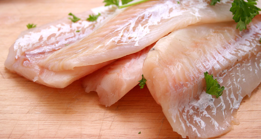 A close-up of raw fish fillets garnished with fresh parsley on a wooden cutting board.