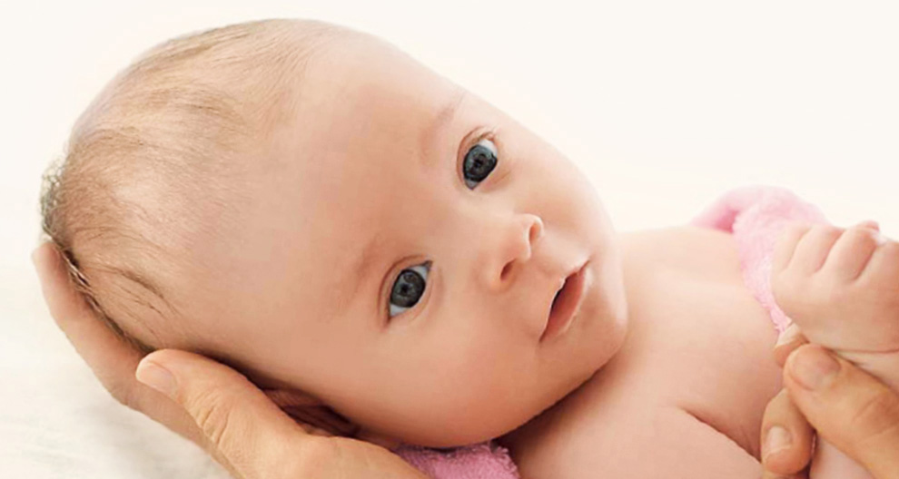 A close-up of a baby's face, with a hand gently cradling the baby's head.