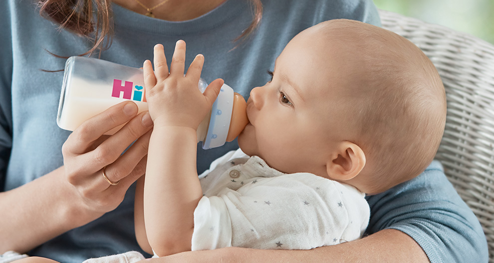 A woman in a blue shirt is feeding a baby with a bottle.