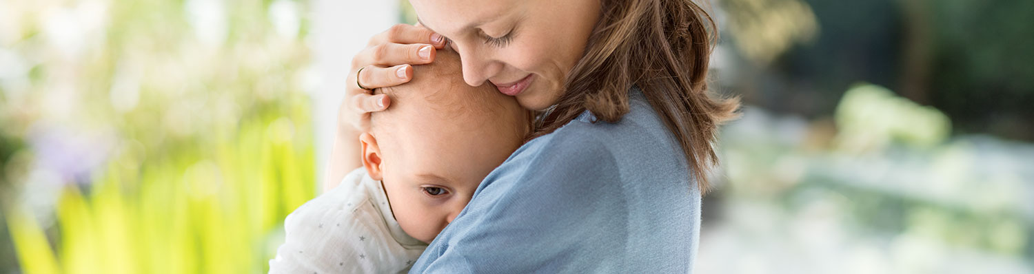 A woman in a blue shirt is holding a baby close to her face, with the baby's head resting against the woman's.