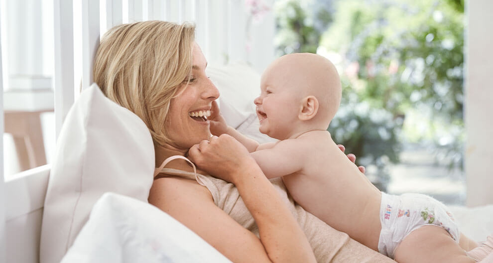 A woman and a baby are lying on a bed, looking at each other.