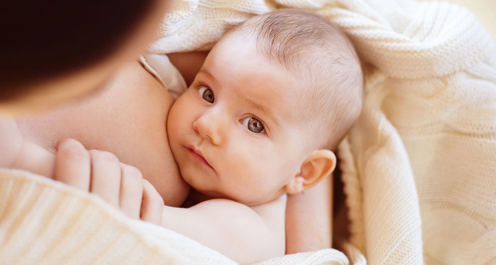 A close-up of a baby's face, partially obscured by a hand, with a soft, neutral background.