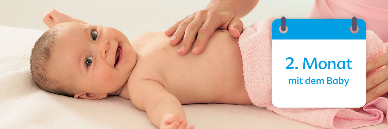 A baby is being dried off by an adult's hands, with a calendar overlay indicating the second month of life.