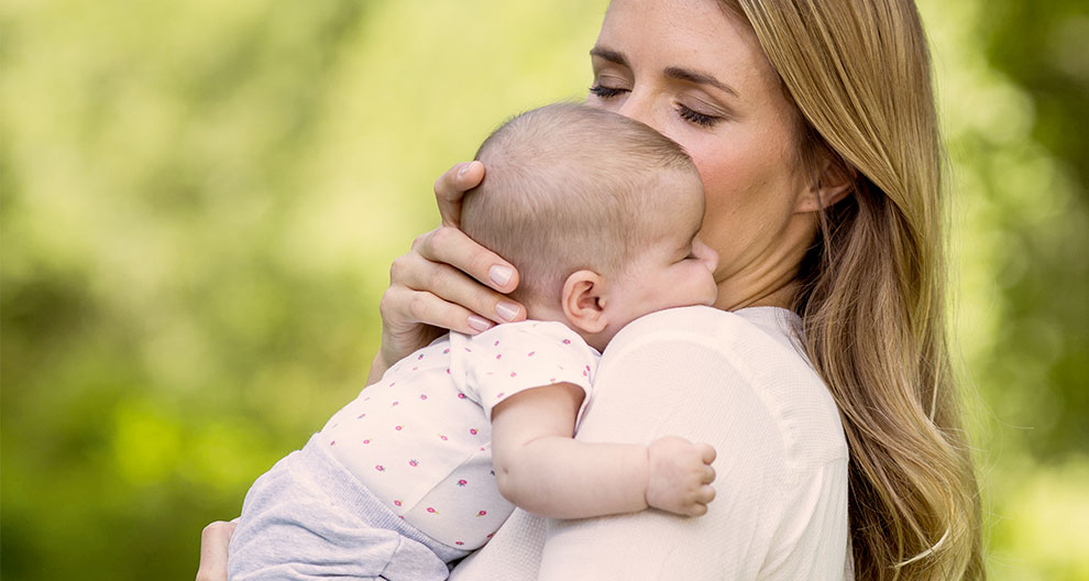 A woman holds a baby in an outdoor setting.
