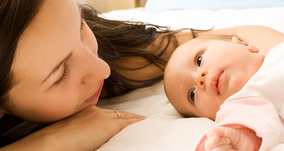 A woman and a baby are lying on a bed, facing each other.
