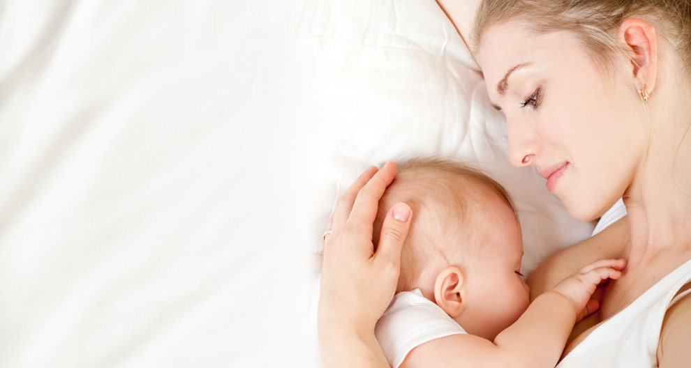 A woman is lying down, cradling a baby close to her chest.