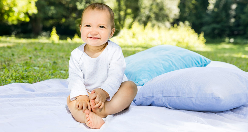 A baby sits on a blanket outdoors.