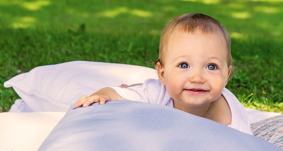 A baby with blue eyes is lying on a blanket outdoors.