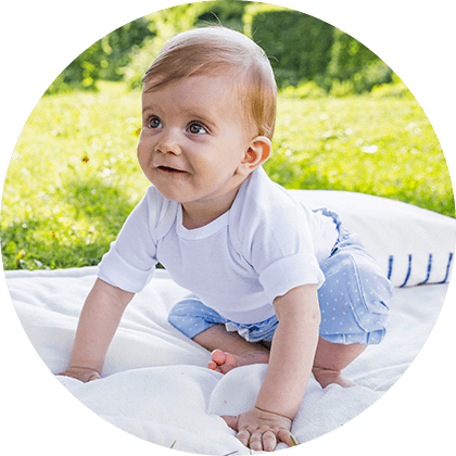 A baby sits on a blanket outdoors.