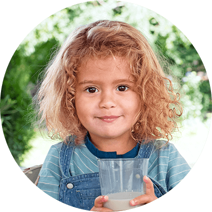A young child with curly hair is holding a glass of a milky beverage.