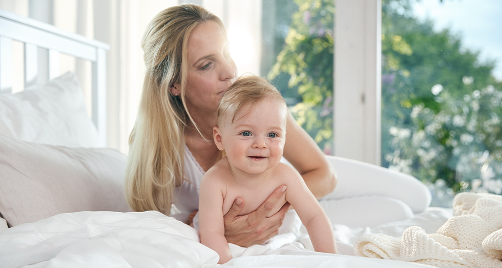 A woman is holding a baby on a bed.
