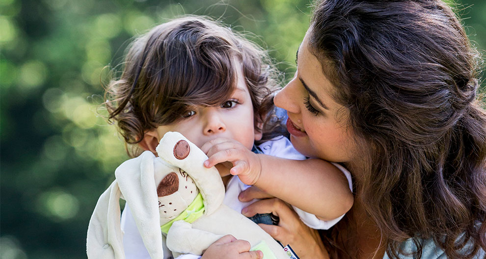 A woman and a child outdoors, with the child holding a stuffed toy.