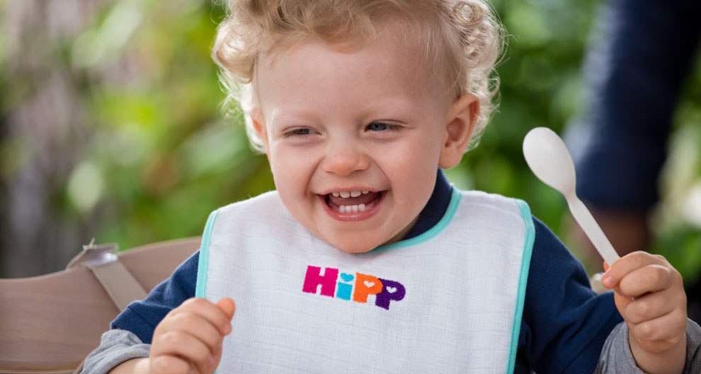 A young child with curly hair is wearing a bib with the word "HIpp" and holding a spoon.