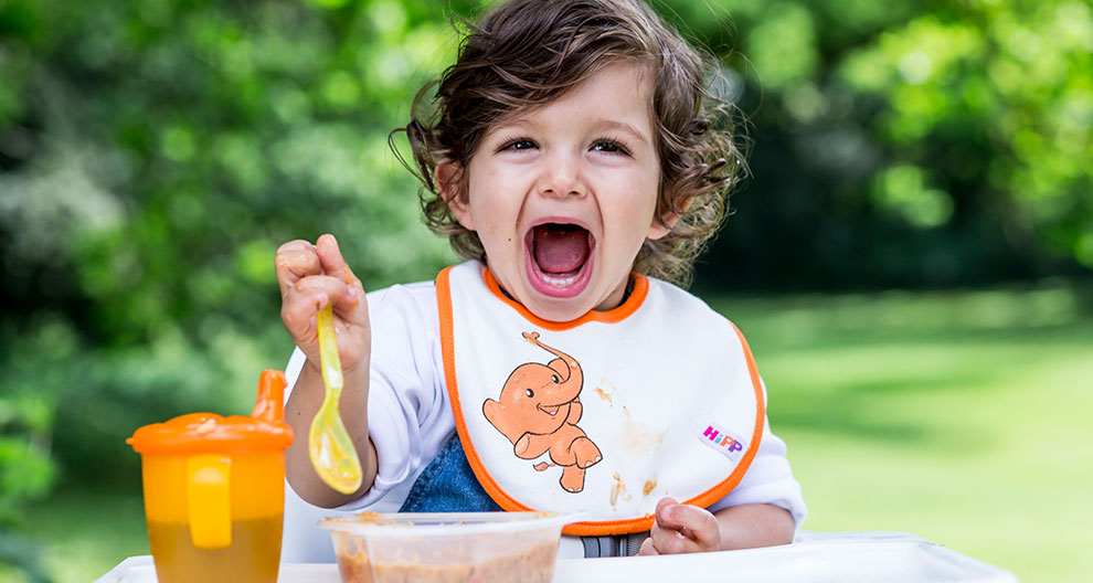 A child with a bib is eating from a container outdoors.