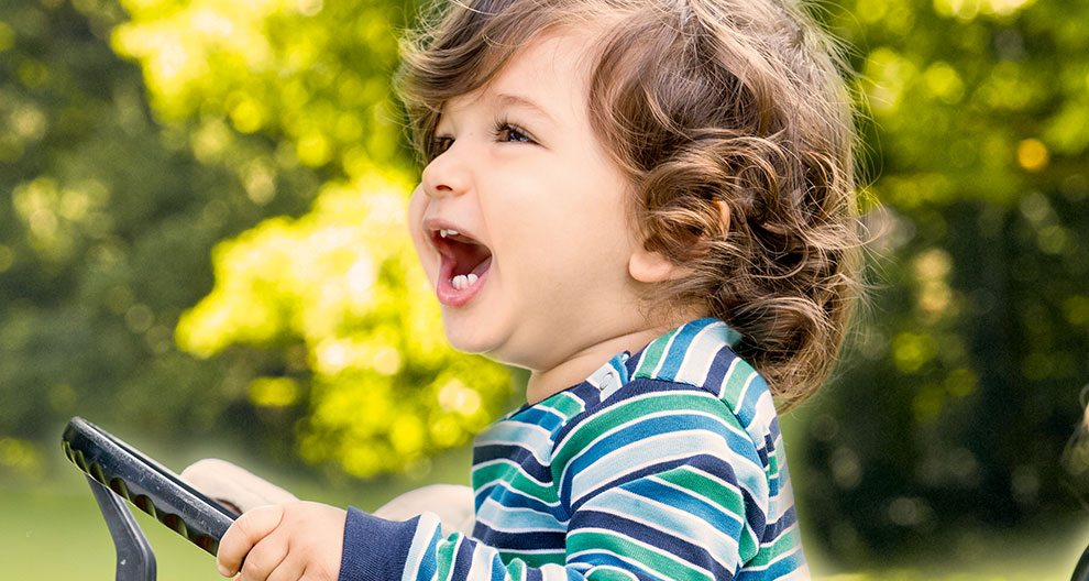 A child in a striped shirt is driving a toy car outdoors.