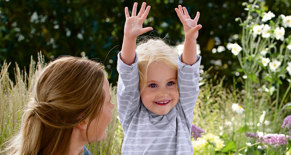 A woman and a young child are outdoors, with the child raising their hands.