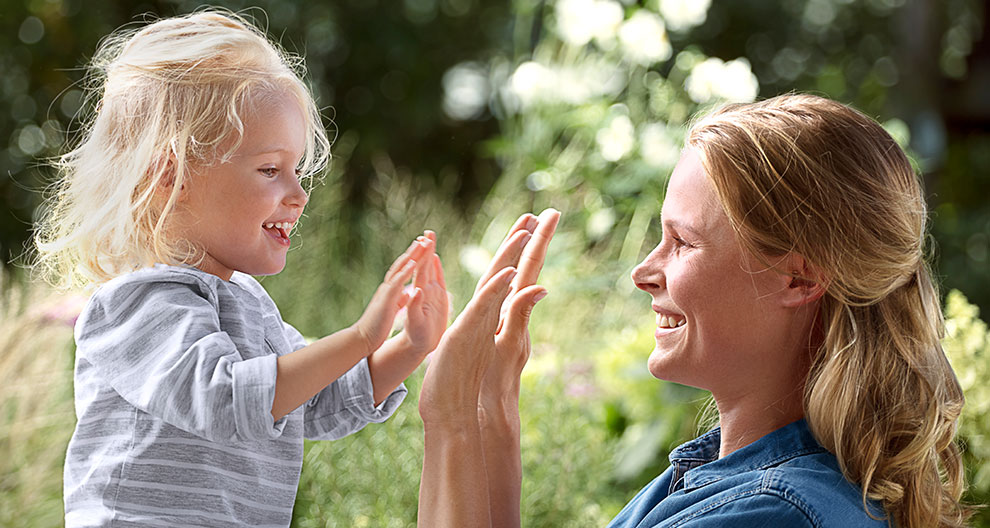 Two individuals, one young and one older, are engaged in a playful hand-clapping activity outdoors.