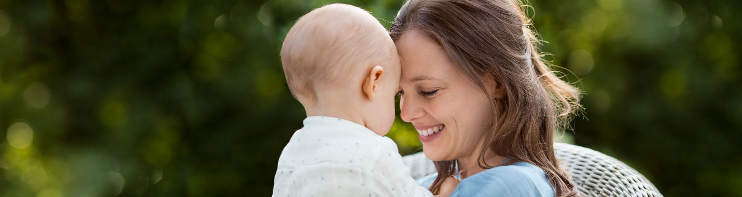 A woman and a baby share a moment of connection outdoors.