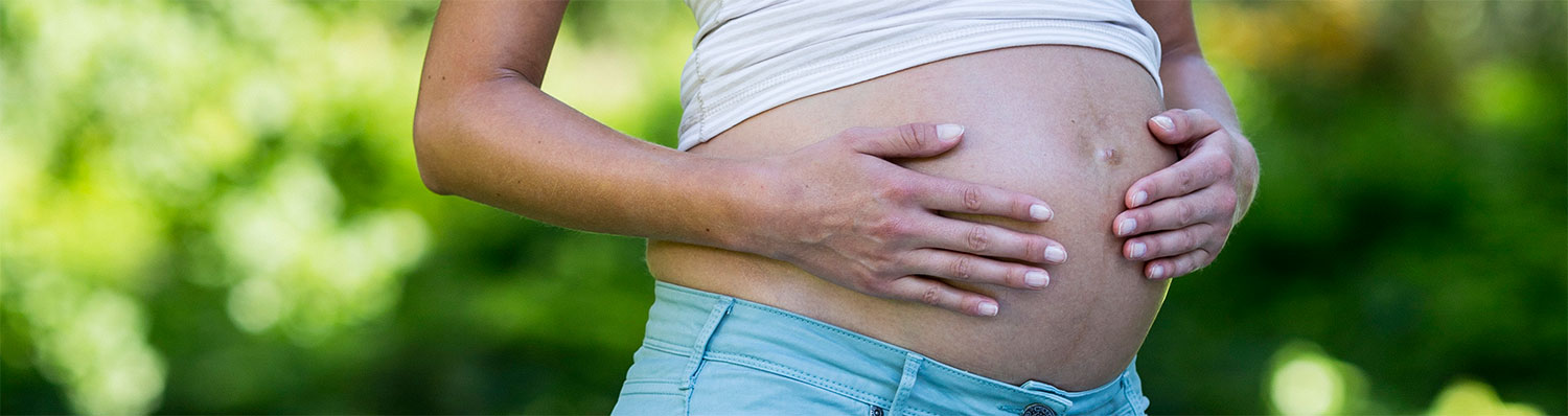 A person's hands are placed on their abdomen, with a blurred green background.