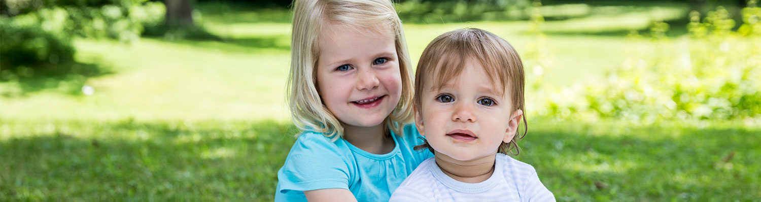 Two children, a girl and a boy, are sitting on grass in a park.