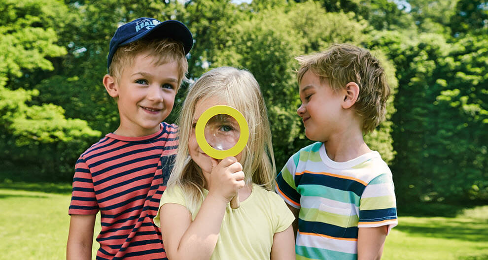 Three children outdoors, one holding a magnifying glass.