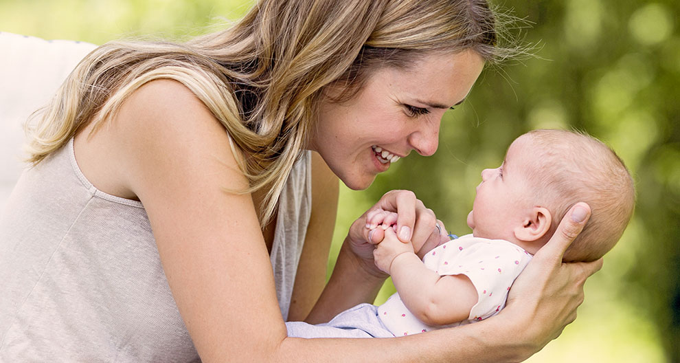 A woman holds a baby outdoors.