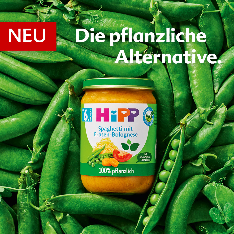 A jar of baby food labeled "Spaghetti mit Erbsen-Bolognese" is placed on a bed of green peas.