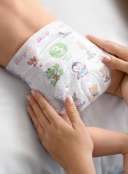 A baby is being dressed in a diaper with various animal prints.