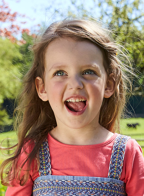 A young girl with a joyful expression is pictured outdoors.