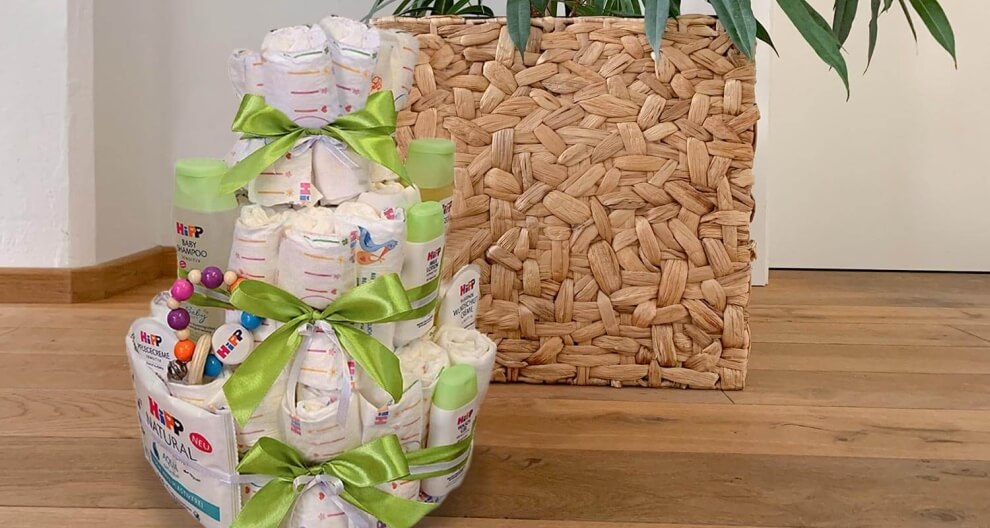 Diaper cake with green ribbons and baby products, next to a woven basket.