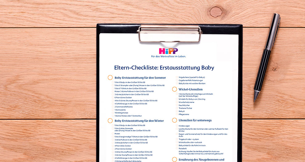 A clipboard with a checklist titled 'Eltern-Checkliste: Erstausstattung Baby' is placed on a wooden surface, accompanied by a pen.