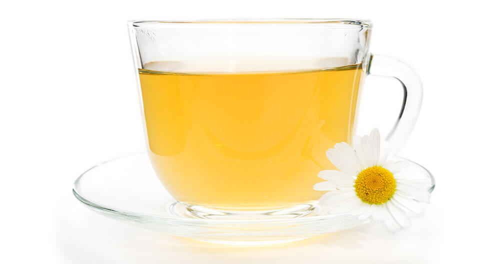 A transparent cup filled with a yellowish liquid sits on a saucer, accompanied by a white daisy with a yellow center.
