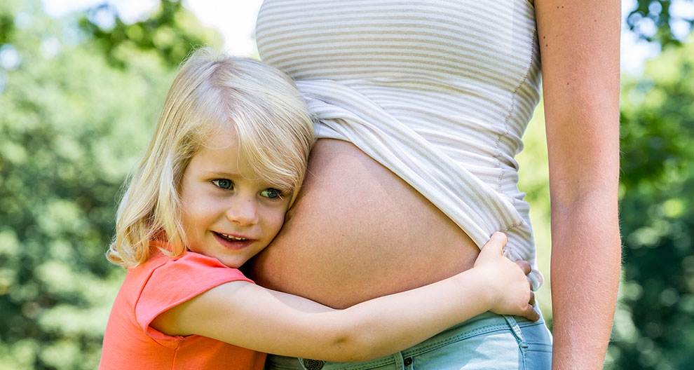 A young girl hugs a pregnant woman.