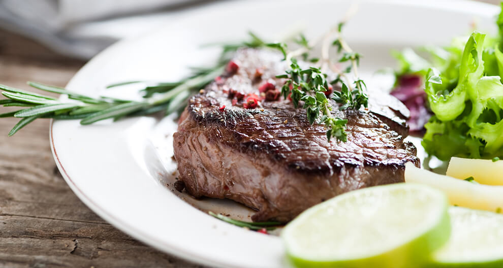 A steak with herbs, salad, and lime slices.