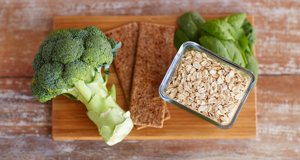 Broccoli, oatmeal, bread, and spinach on a wooden surface.
