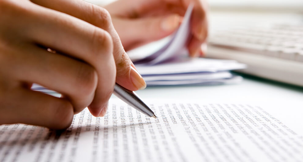 A hand holds a pen, hovering over a page of text.