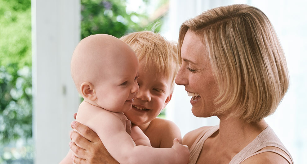 A woman lovingly interacts with two children.